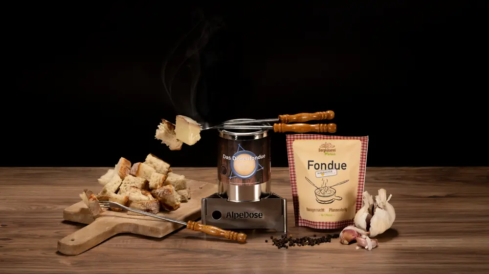 Das Dosenfondue von AlpeDose mit Brot, Fonduebeutel und Knoblauch auf einem Holztisch.