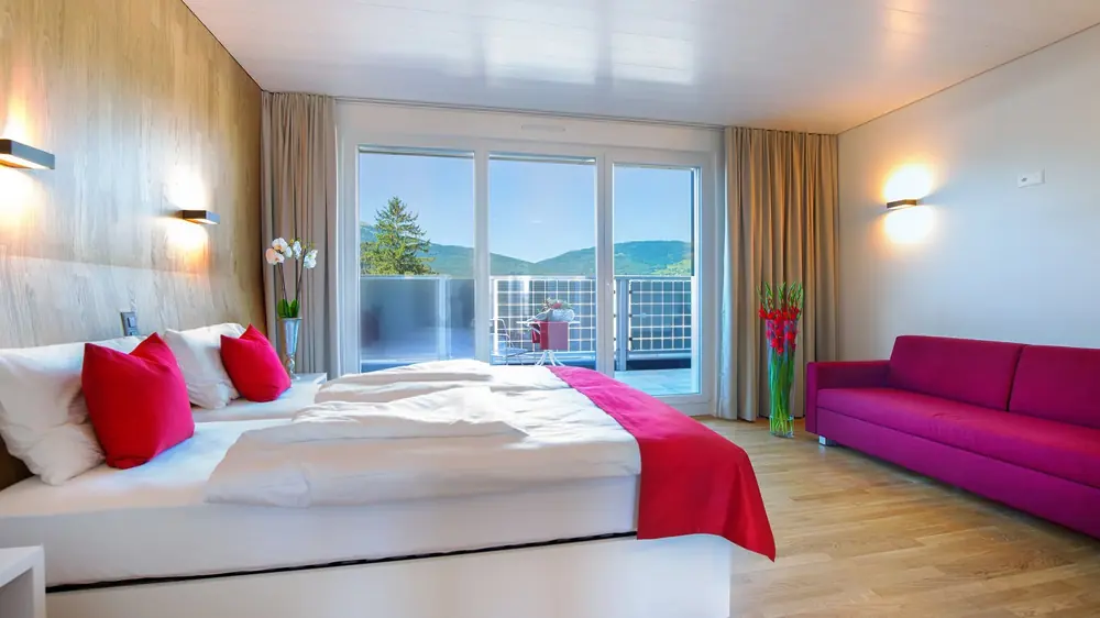 Ein Zimmer im Hotel Restaurant RHY mit Bett, roten Kissen und Blick auf den Balkon.